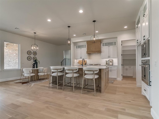 kitchen featuring baseboards, a kitchen bar, light wood-style floors, an island with sink, and appliances with stainless steel finishes