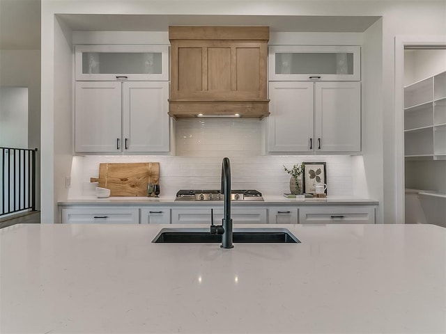 kitchen featuring glass insert cabinets, light stone counters, a sink, and backsplash