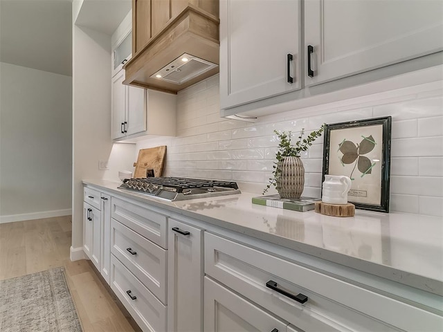 kitchen with baseboards, light wood-style floors, stainless steel gas stovetop, decorative backsplash, and custom range hood