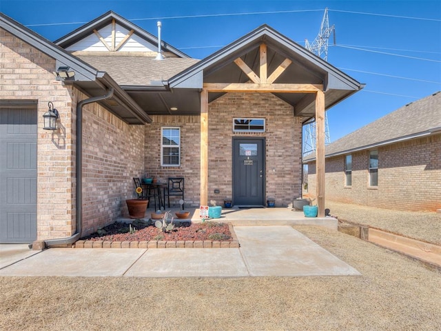 property entrance with brick siding, an attached garage, and a shingled roof