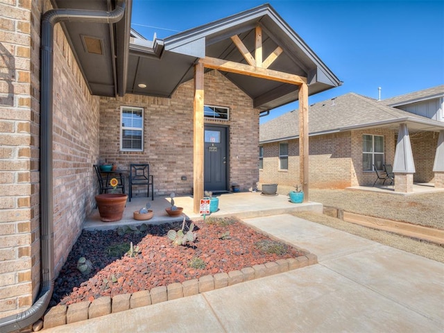 doorway to property with brick siding, a porch, and roof with shingles