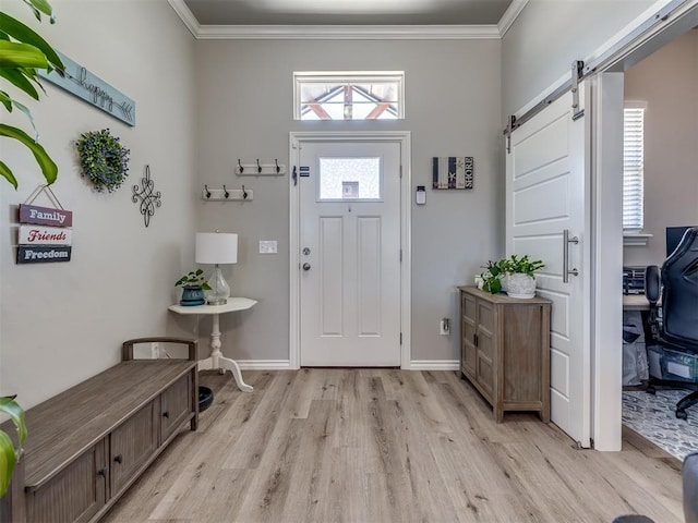 entryway featuring a barn door, baseboards, crown molding, and light wood finished floors