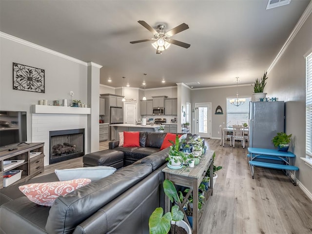 living room featuring baseboards, light wood-type flooring, ornamental molding, ceiling fan with notable chandelier, and a fireplace