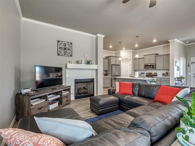 living room with visible vents, light wood-style flooring, a ceiling fan, ornamental molding, and a fireplace