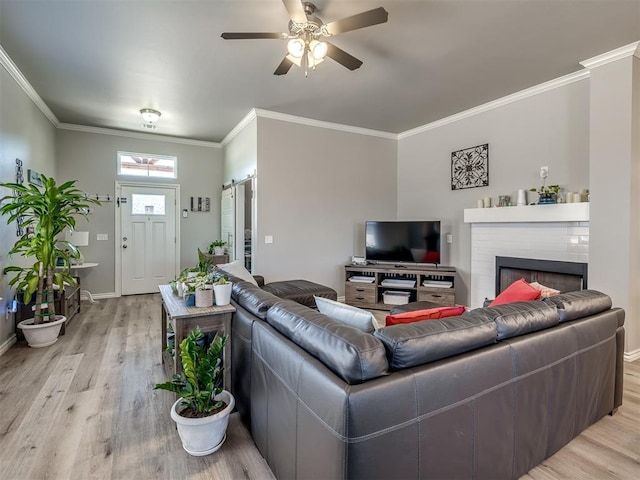 living area with a ceiling fan, baseboards, light wood finished floors, a fireplace, and crown molding