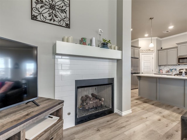 living room with visible vents, light wood-style flooring, recessed lighting, a fireplace, and crown molding