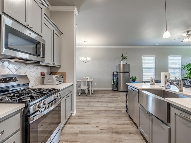 kitchen featuring tasteful backsplash, ornamental molding, gray cabinets, appliances with stainless steel finishes, and ceiling fan with notable chandelier