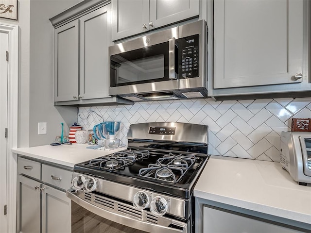 kitchen featuring gray cabinets, backsplash, appliances with stainless steel finishes, a toaster, and light countertops