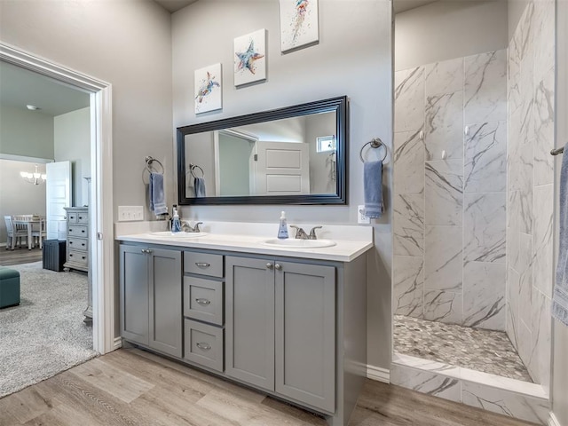 full bathroom featuring a chandelier, double vanity, a tile shower, wood finished floors, and a sink