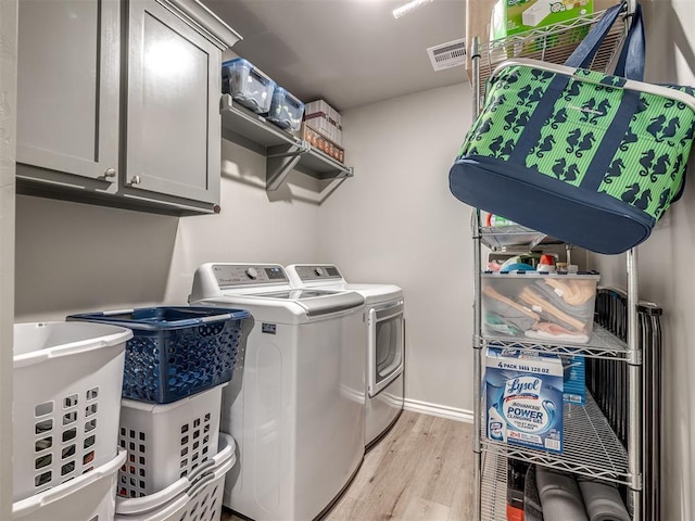 clothes washing area with cabinet space, light wood-style flooring, separate washer and dryer, and visible vents