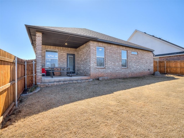 rear view of property with a patio area, a fenced backyard, a shingled roof, and brick siding