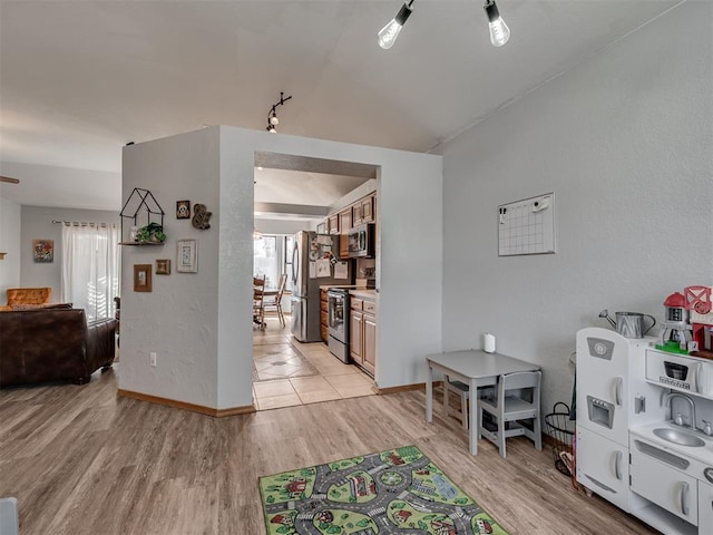 interior space featuring lofted ceiling, a textured wall, baseboards, and light wood finished floors