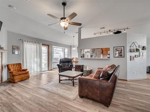 living area with light wood finished floors, visible vents, baseboards, ceiling fan, and vaulted ceiling