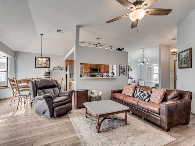 living area featuring vaulted ceiling, light wood finished floors, visible vents, and a wealth of natural light