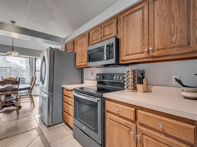 kitchen with light tile patterned floors, stainless steel appliances, light countertops, decorative light fixtures, and brown cabinets