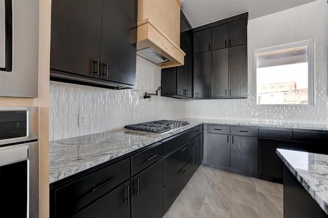 kitchen featuring tasteful backsplash, light stone counters, custom range hood, and dark cabinets