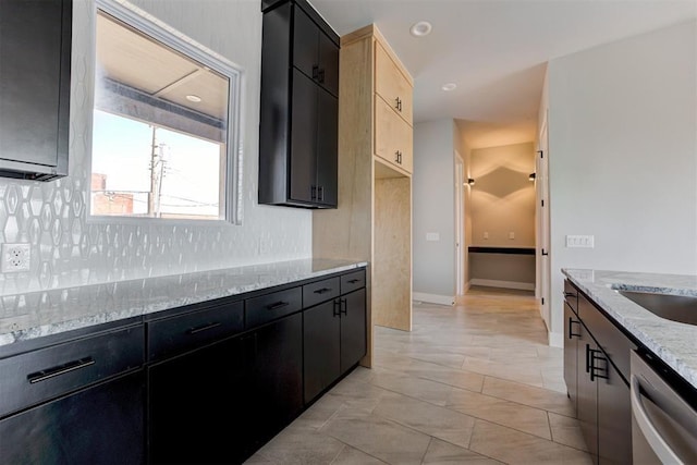 kitchen featuring light stone counters, a sink, tasteful backsplash, dishwasher, and dark cabinets