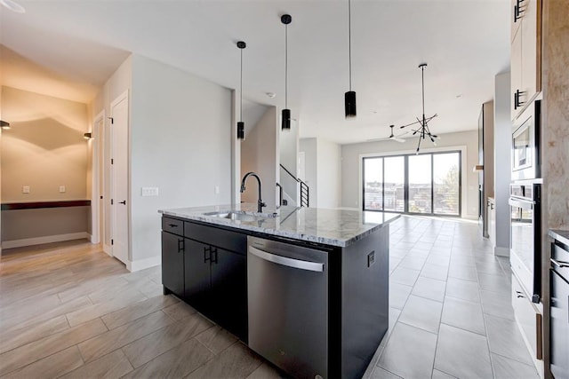 kitchen featuring dark cabinetry, a kitchen island with sink, a sink, appliances with stainless steel finishes, and open floor plan