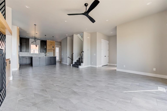 unfurnished living room featuring stairs, baseboards, and ceiling fan