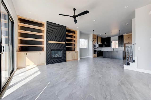 unfurnished living room featuring built in shelves, ceiling fan, stairway, a fireplace, and a sink