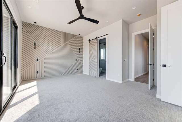 unfurnished bedroom featuring carpet flooring, baseboards, a barn door, and a ceiling fan