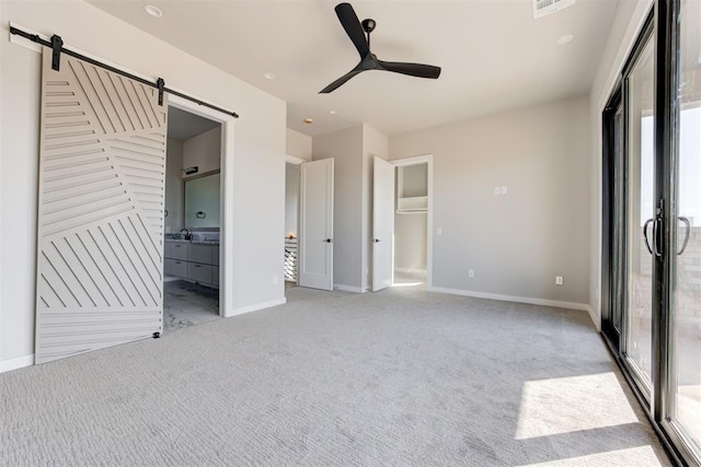 unfurnished bedroom with a barn door, light carpet, baseboards, and connected bathroom