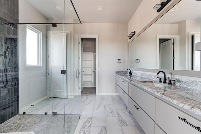 bathroom featuring marble finish floor, a sink, a shower stall, double vanity, and baseboards