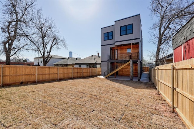 back of property with stucco siding, a lawn, a fenced backyard, and stairs