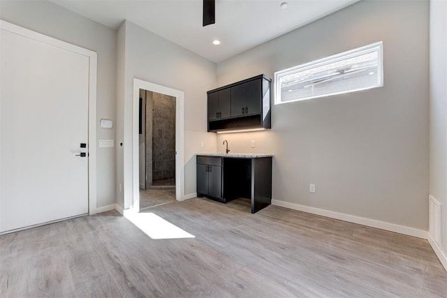 kitchen featuring dark cabinets, baseboards, light wood-style flooring, and a ceiling fan