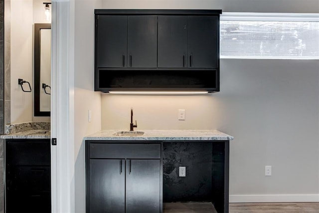 interior space with a sink, indoor wet bar, baseboards, and wood finished floors