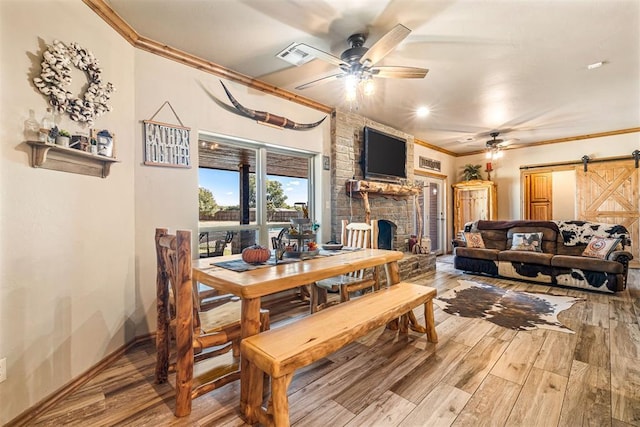 dining area with a ceiling fan, ornamental molding, a barn door, light wood-type flooring, and a large fireplace