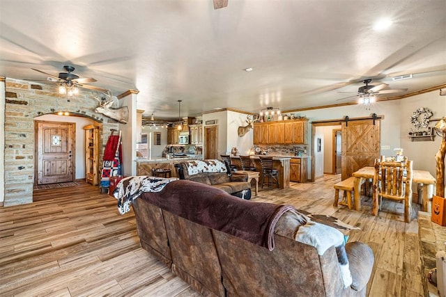 living area featuring ceiling fan, light wood-style floors, a barn door, and ornamental molding