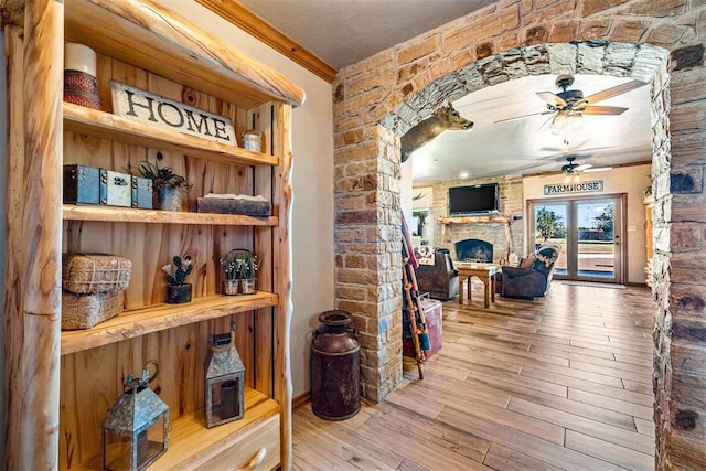 interior space featuring wood finished floors, a fireplace, arched walkways, ceiling fan, and crown molding