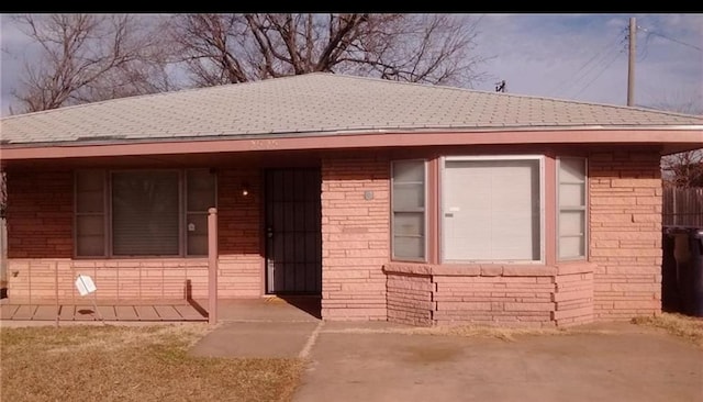 single story home featuring brick siding, roof with shingles, and fence