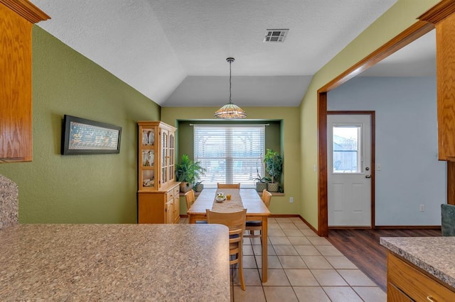 dining space featuring visible vents, a textured ceiling, light tile patterned floors, baseboards, and vaulted ceiling