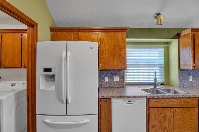 kitchen featuring white appliances, washer / dryer, a sink, brown cabinets, and backsplash