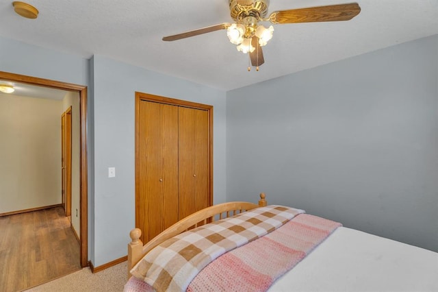 bedroom with a closet, light colored carpet, baseboards, and a ceiling fan