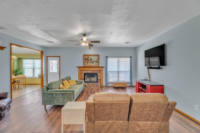 living area with a fireplace, a textured ceiling, ceiling fan, and wood finished floors