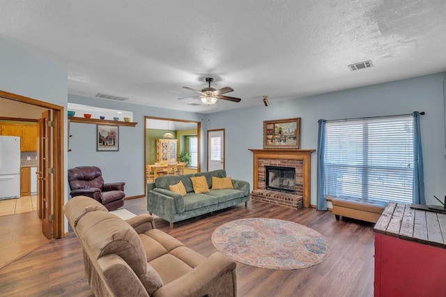 living room with ceiling fan, visible vents, wood finished floors, and a fireplace