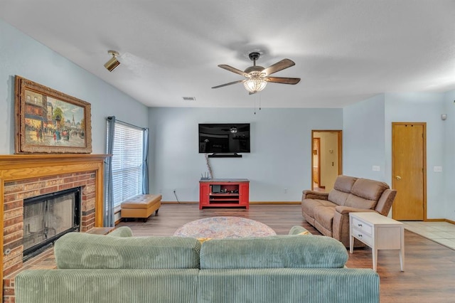 living room featuring visible vents, a brick fireplace, baseboards, wood finished floors, and a ceiling fan