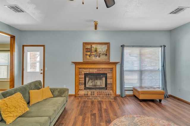 living area featuring visible vents, a brick fireplace, and wood finished floors