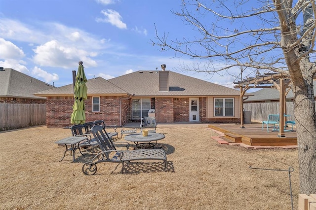 rear view of house featuring a pergola, a fenced backyard, roof with shingles, a wooden deck, and brick siding