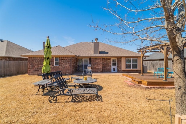 rear view of property featuring brick siding, a shingled roof, a wooden deck, a fenced backyard, and a pergola