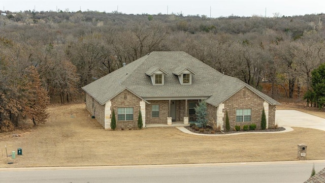 view of front facade with a porch, brick siding, roof with shingles, and a wooded view