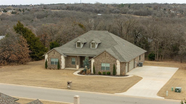 view of front of home featuring brick siding, an attached garage, roof with shingles, central AC unit, and driveway