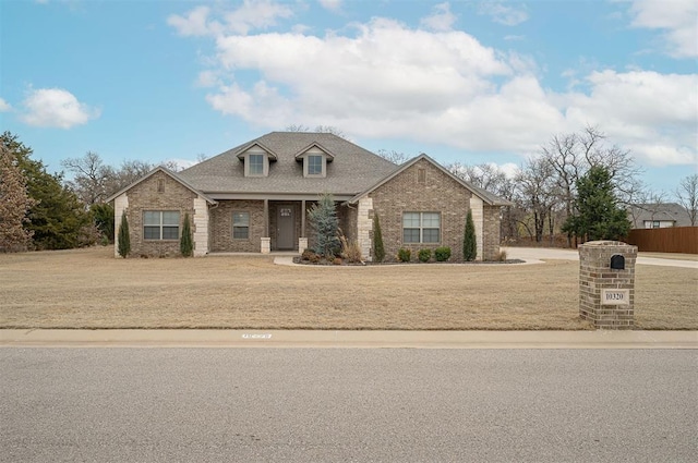 view of front facade with brick siding, a front yard, and a shingled roof