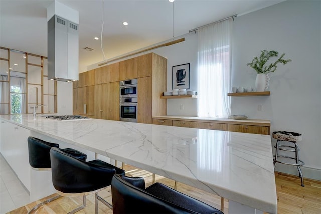 kitchen featuring light stone countertops, stainless steel double oven, modern cabinets, brown cabinets, and island range hood