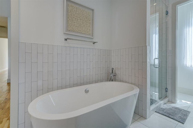 full bath with a wainscoted wall, a freestanding bath, tile patterned flooring, a shower stall, and tile walls