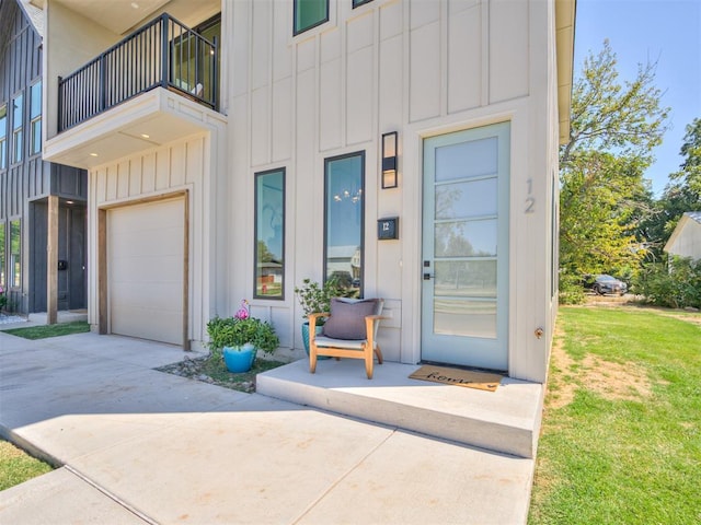 view of exterior entry featuring a balcony, a yard, concrete driveway, a garage, and board and batten siding