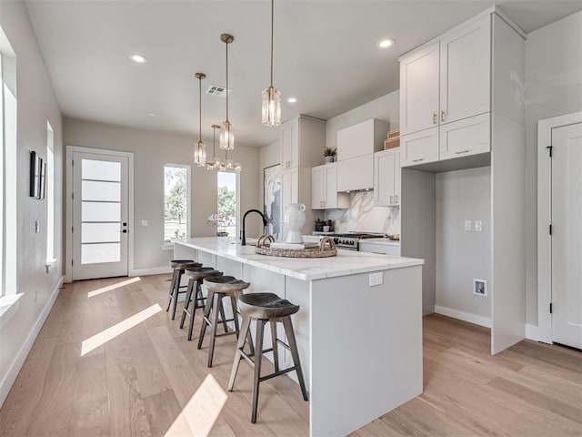12 S Howard St, Edmond, OK 73003 - kitchen with visible vents, a spacious island, backsplash, white cabinetry, and light wood-style floors